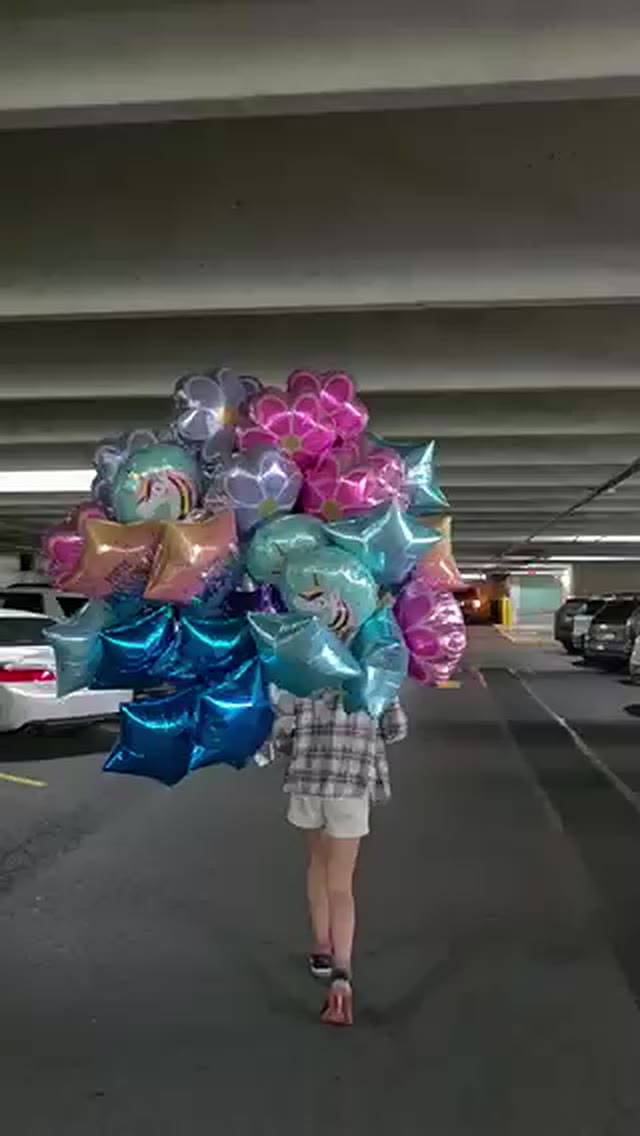 Ashton carrying a giant bundle of shiny star and flower balloons through a parking garage
