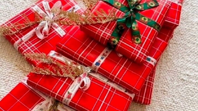 Christmas gifts for women at a shelter, wrapped in red plaid paper with festive ribbons and gold glitter sprigs.