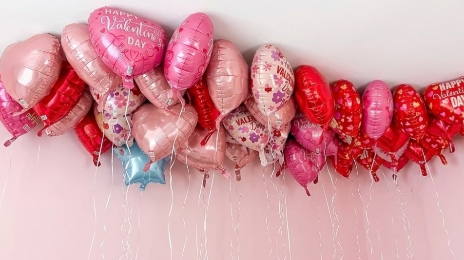 Dozens of pink and red heart-shaped Valentine's balloons float near the ceiling with ribbons hanging below.