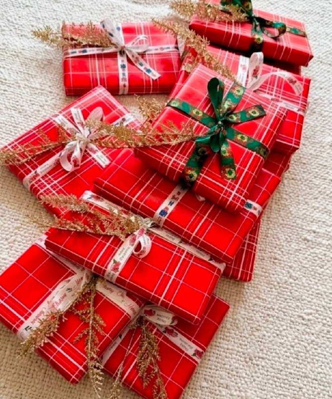 A pile of gifts wrapped in red plaid Christmas paper with ribbons and gold glitter sprigs.