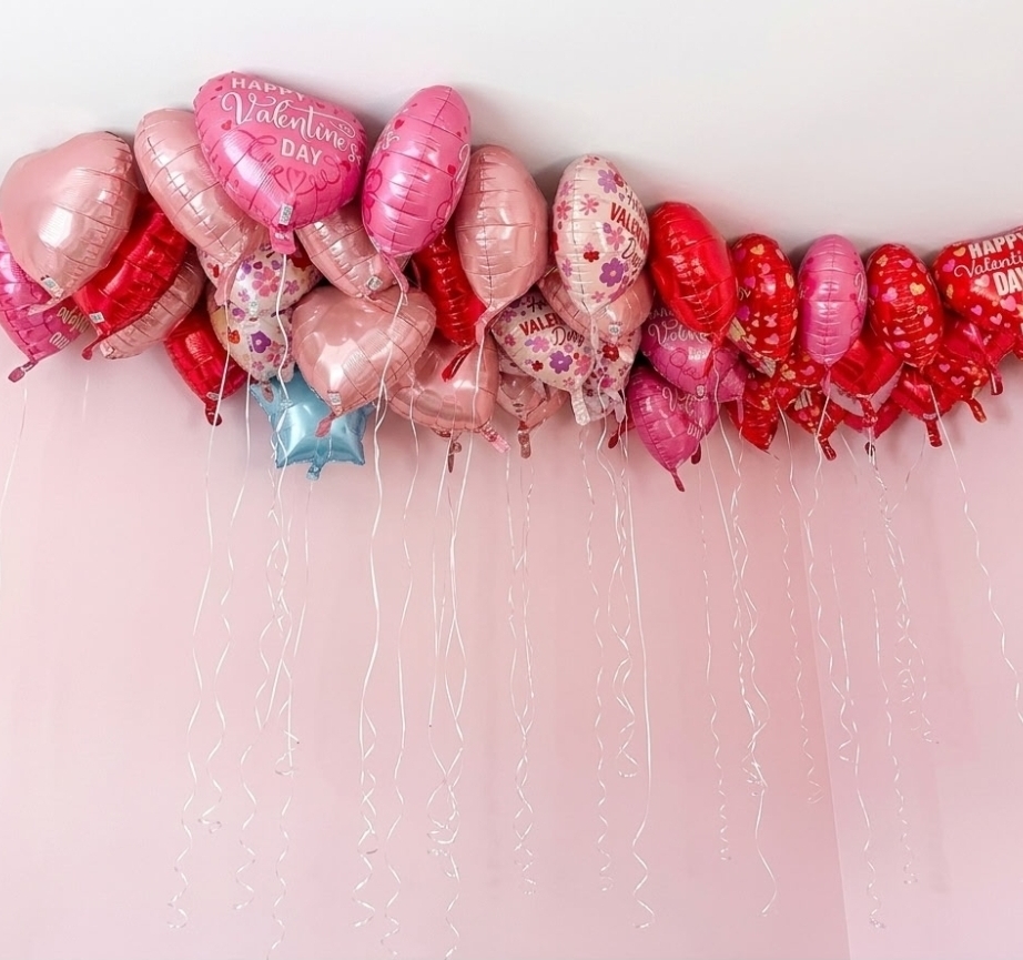 Dozens of pink and red heart-shaped Valentine's balloons floating against a ceiling with ribbons hanging down.
